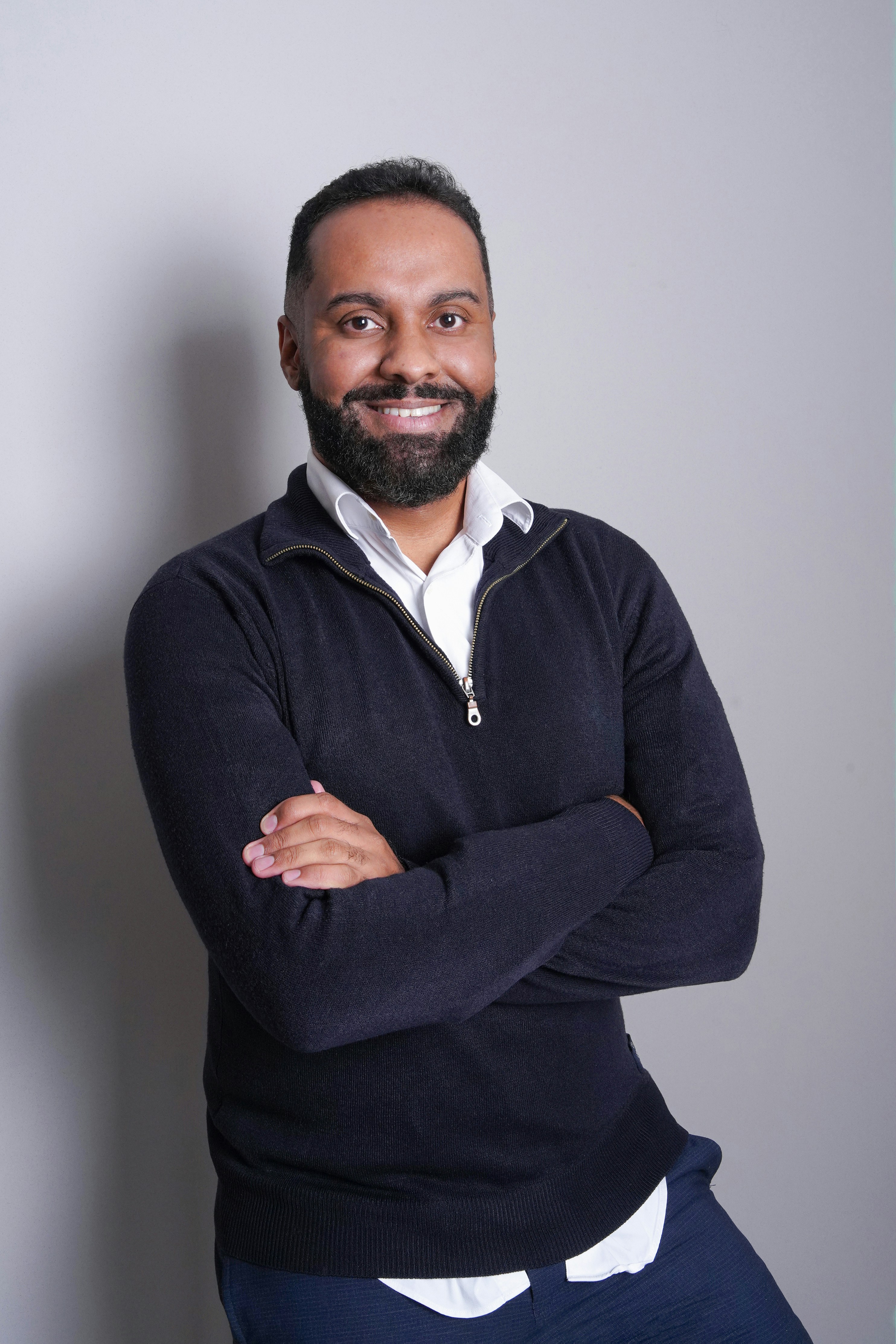 Smiling man with a beard, arms crossed, wearing a black sweater.